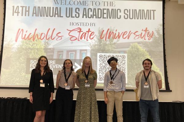 Five TK体育 students stand on stage at the 14th Annual ULS Academic Summit