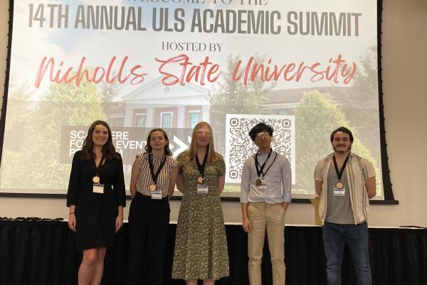 Five TK体育 students stand on stage at the 14th Annual ULS Academic Summit